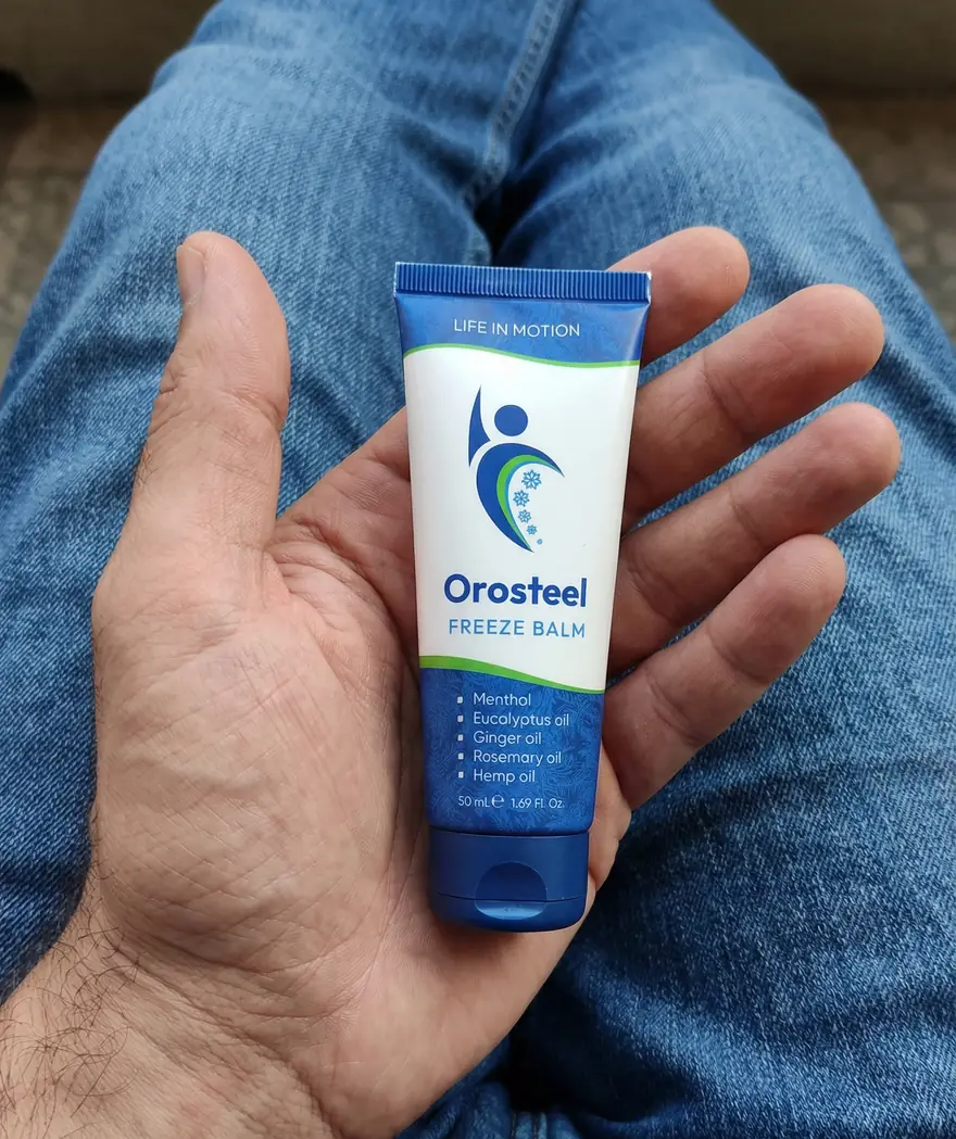 Tuba chladivého balzámu Orosteel Freeze Balm na dlani nad kolenem v džínách